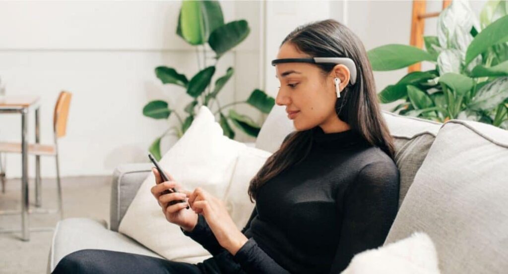 زن روی مبل در حال کار با موبایل و هدبند دیجیتالی روی سر